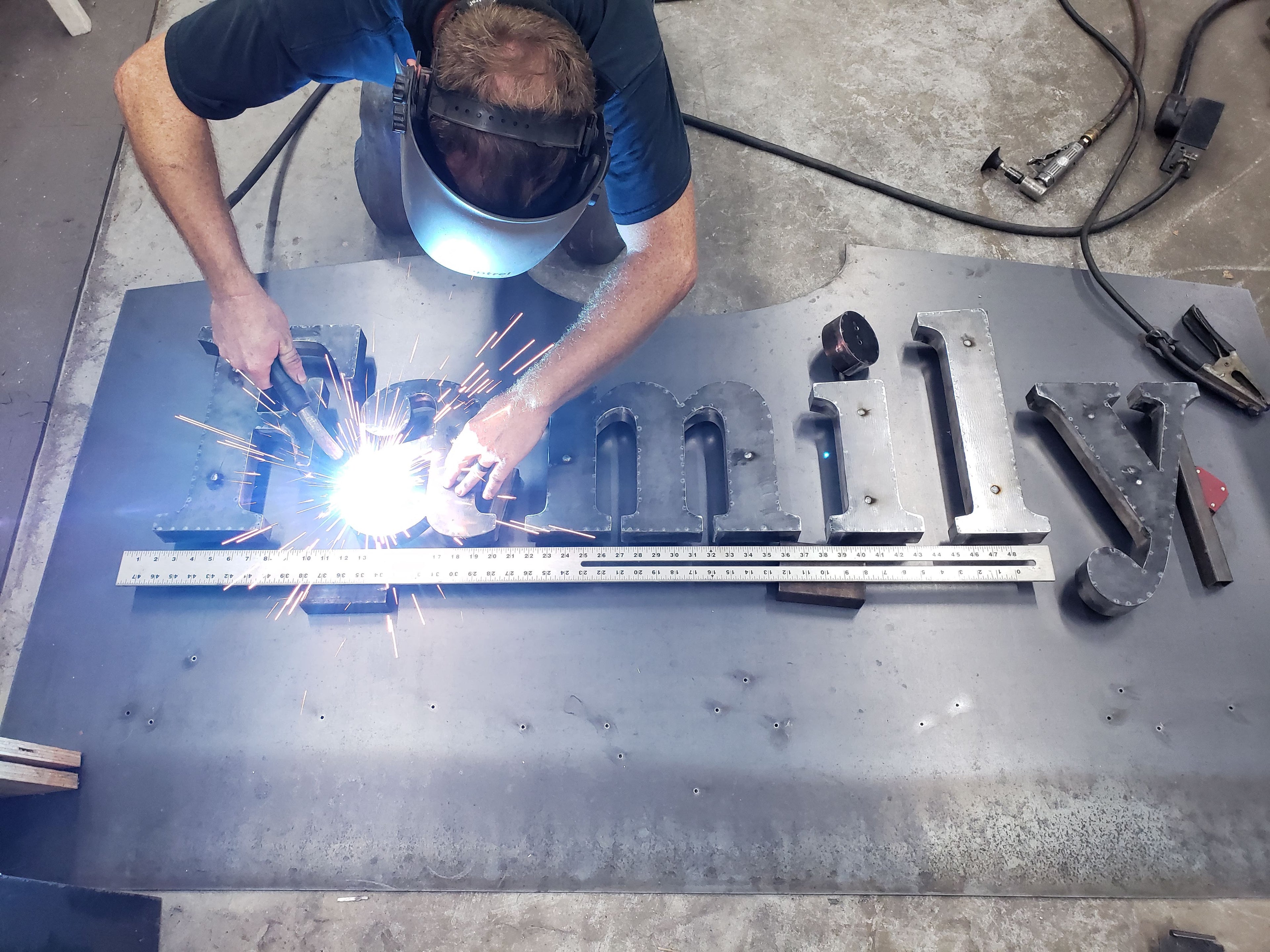 man welding large custom metal business sign