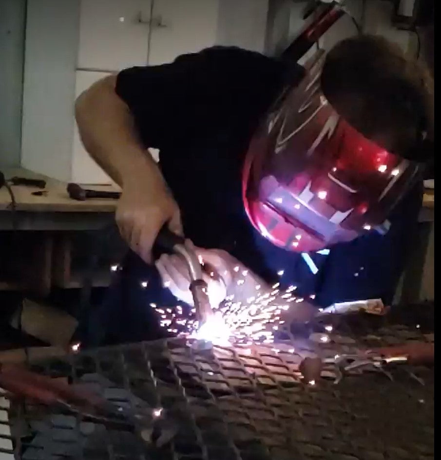 man repairing metal by welding wearing welding helmet